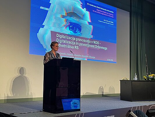 Saša Levstik na predavateljskem odru s projekcijo naslovne teme v ozadju.